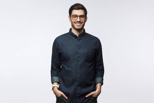 handsome smiling young man in casual denim shirt and trendy glasses standing isolated on gray background - shirt lifestyles close up cheerful imagens e fotografias de stock