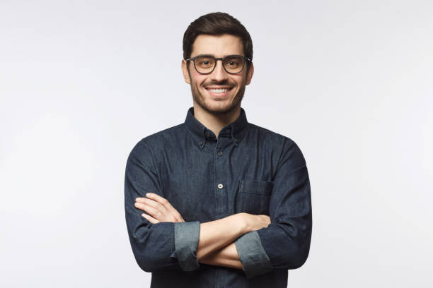 молодой человек в джинсовой рубашке, стоящей со скрещенными руками, изолированный на сером фоне - male fashion model adult human arm стоковые фото и изображения
