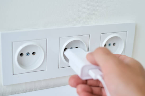 男性の手はソケットに白いプラグを置きます - electric plug outlet pulling electricity ストックフォトと画像