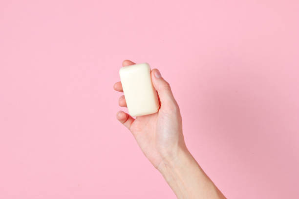 Female hand holding piece of soap against pink background. Top view Female hand holding piece of soap against pink background. Top view soap sud photos stock pictures, royalty-free photos & images