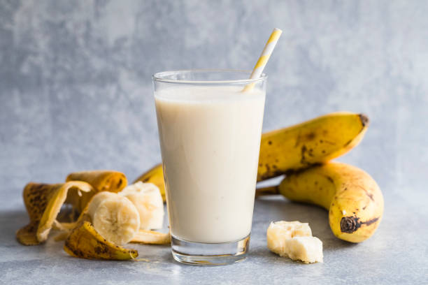 Banana smoothie Banana smoothie of organic bananas. There is a high glass filled with banana smoothie in the centre, and bananas and banana peels around the drink. With an environmentally friendly paper straw. blended drink photos stock pictures, royalty-free photos & images