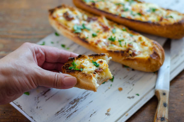 The cheese filled baguette breads on the table in kitchen,close up.The woman is holding in her hand a piece of bread.