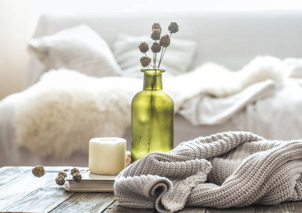 Still life home decor on a wooden table in the living room. decorative bottle with flowers and a candle near a knitted sweater.