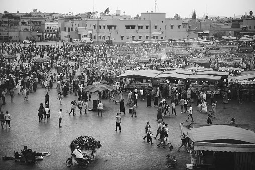A black and white shot of Marrakech market from a high angle, with smoke rising from the food stalls and lots of people walking around. Marrakech, Morocco - September 2017.