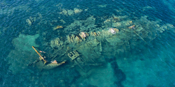 View from above, stunning aerial view of a wreck inside the Marine Protected Area of Tavolara. Some people snorkel in an emerald green sea. Sardinia, Italy.