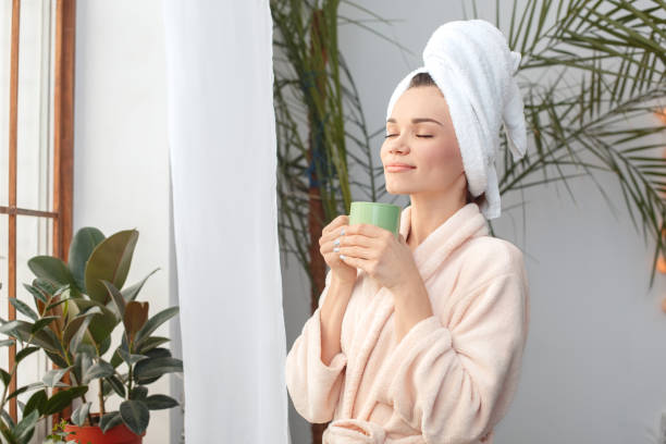 Young woman at home beauty care standing in towel drinking coffee closed eyes smiling satisfied Young woman rest at home beauty care standing near window wearing towel holding cup drinking hot coffee closed eyes smiling satisfied home pampering stock pictures, royalty-free photos & images
