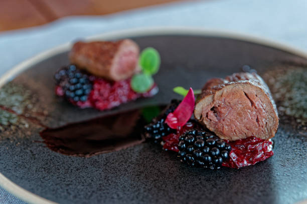 Venison fillet with beetroot carpaccio and blackberries on dark plate, close-up shot