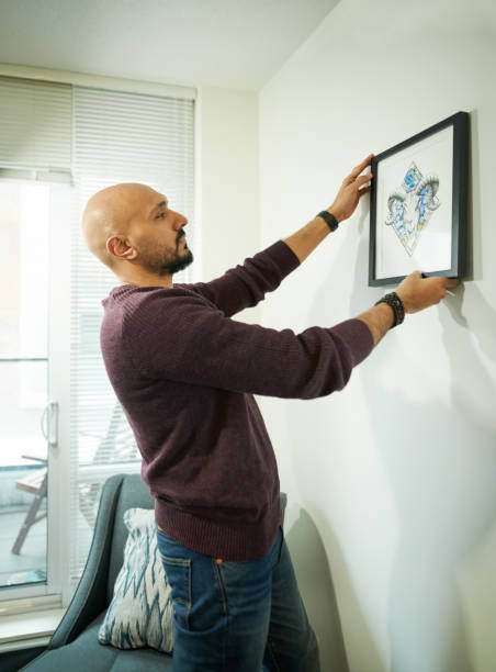 Aligning the frame Shot of young man hanging a picture frame on the wall of his new apartment hanging art on wall stock pictures, royalty-free photos & images