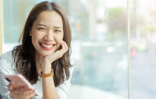 close up young business beautiful asian woman smiling and holding mobile phone with happiness at coffee shop in relaxing time for millennial lifestyle concept