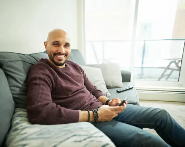 Shot of smiling young man sitting on couch with a mobile phone