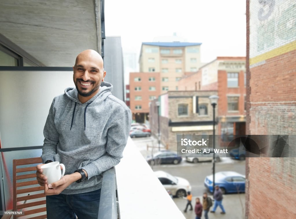 Best place to have a coffee Shot of smiling young man standing in the balcony with cup of coffee Men Stock Photo