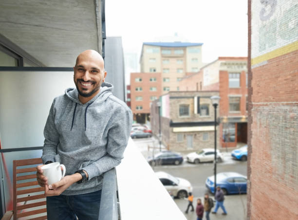 Best place to have a coffee Shot of smiling young man standing in the balcony with cup of coffee balding photos stock pictures, royalty-free photos & images