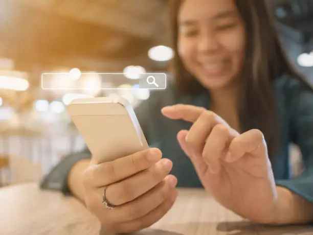 Photo of The girl smiles and uses a smartphone to find what you are interested. Searching information data on internet networking concept