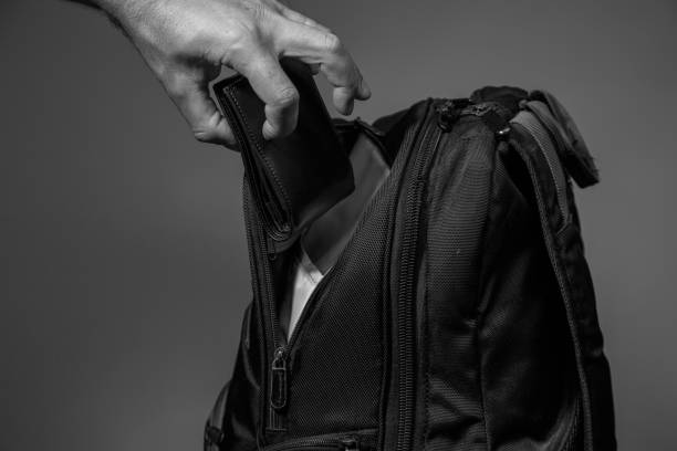 istock Black and white photo of a thief's hand pulling a purse from a backpack on a gray background 1170234298