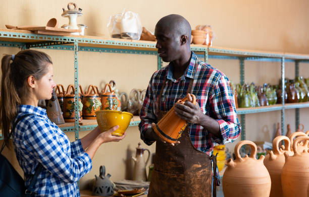 Shop assistant helping girl choose ceramics Afro male shop assistant helping girl choose ceramic production in pottery shop kenyan man stock pictures, royalty-free photos & images