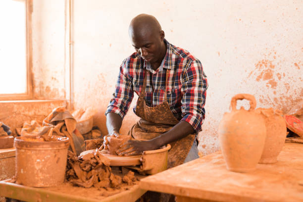 Man making ceramics on pottery wheel Skilled african american potter working on potters wheel making clay products in pottery workshop hobbyist stock pictures, royalty-free photos & images