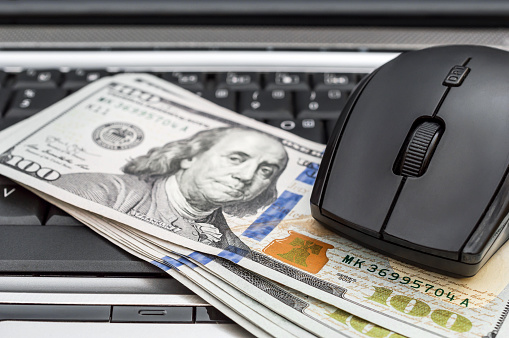 Computer mouse with dollar bills on laptop keyboard.