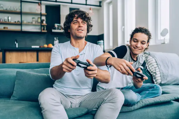 Father and teenager son playing video game at home
