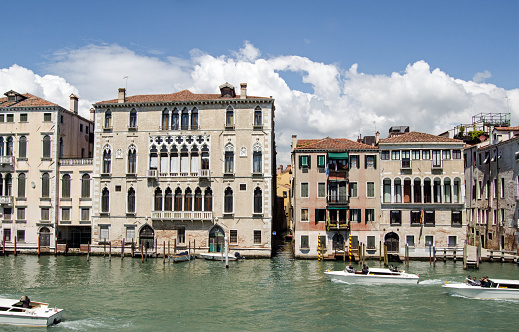 Venice, Italy - May 16, 2019:  View on a sunny Spring day across the Grand Canal of Venice looking towards the larger Palazzo Querini Dubois on the left and the smaller Palazzo Dona on the right as taxis transport eager tourists along the water.