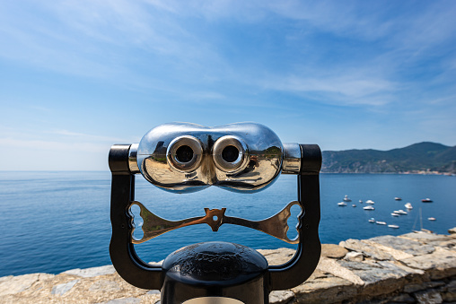 Coin operated electronic binoculars for tourists on a blurred seascape with boats. Vernazza village, Cinque Terre, National park in Liguria, La Spezia, Italy, Europe. UNESCO world heritage site