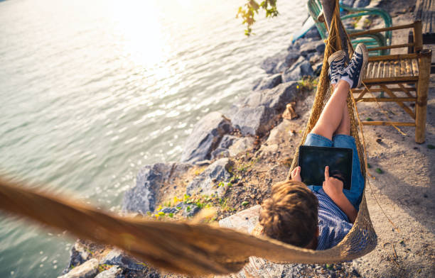 Chilling out in hammock near sea at sunset Chilling out in hammock near sea at sunset hammock men lying down digital tablet stock pictures, royalty-free photos & images