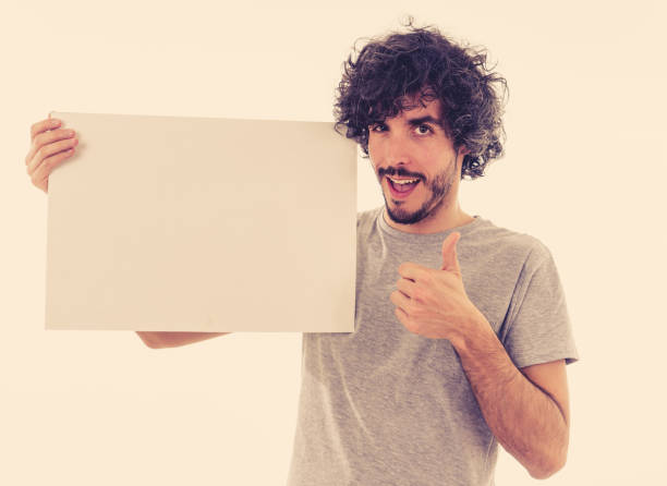 istock Funny and good looking man showing and pointing at blank board with copy space for text. Friendly and excited young stylish man holding blank poster for advertisement. In marketing concept. 1170262154