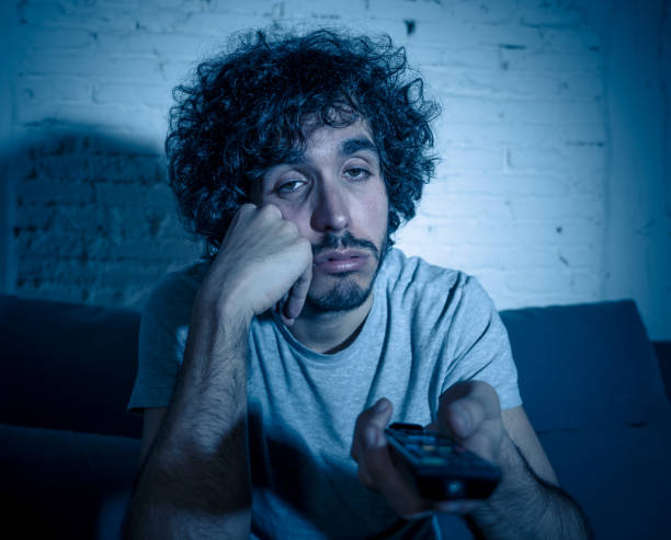 istock Bored man watching sitcom or series falling asleep on sofa late at night. young male zapping and changing TV channels looking for show or movie killing time at night feeling restless 1170262192