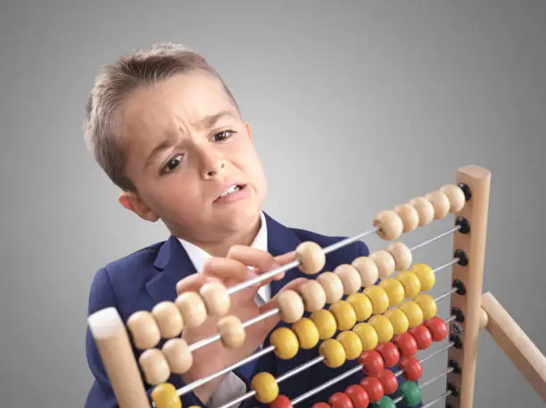 Young boy accountant businessman does math calculation on a abacus looking confused