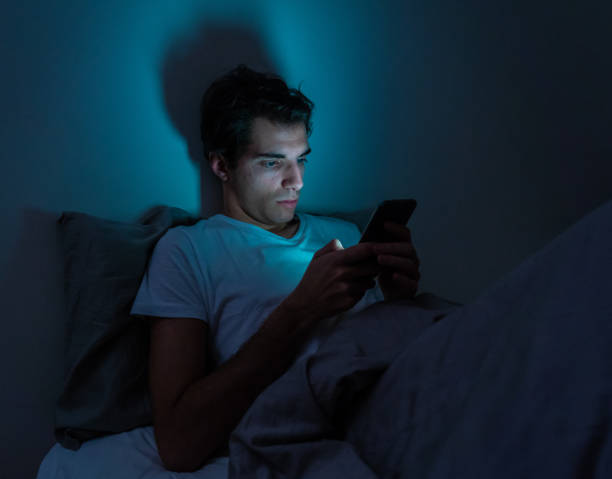 el hombre adicto a los teléfonos inteligentes se despierta hasta altas horas de la noche en la cama usando los "me gusta" y seguidores de la verificación del teléfono móvil, chateando, coqueteando, saliendo en las redes sociales. adicción a internet y - working bed smart phone bedroom fotografías e imágenes de stock