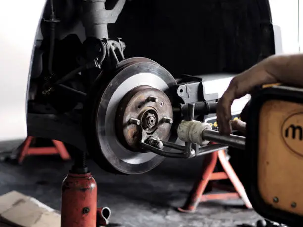 Man is working in garage. Brake disc with grinding machine and vehicle brake-disc. Disc brake system repair