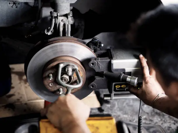 Man is working in garage. Brake disc with grinding machine and vehicle brake-disc. Disc brake system repair