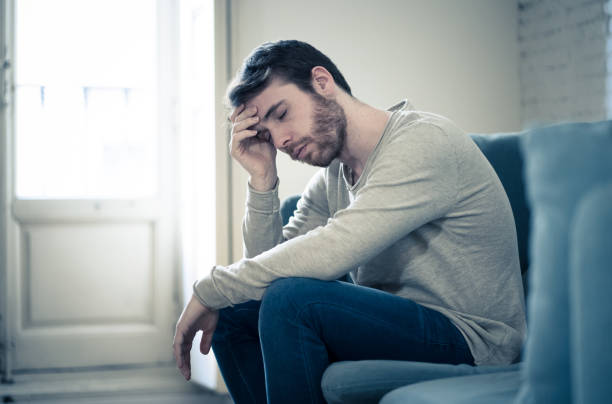 Unhappy depressed caucasian male sitting and lying in living room couch feeling desperate a lonely suffering from depression. In stressed from work, anxiety, heartbroken and men Health care concept. stock photo