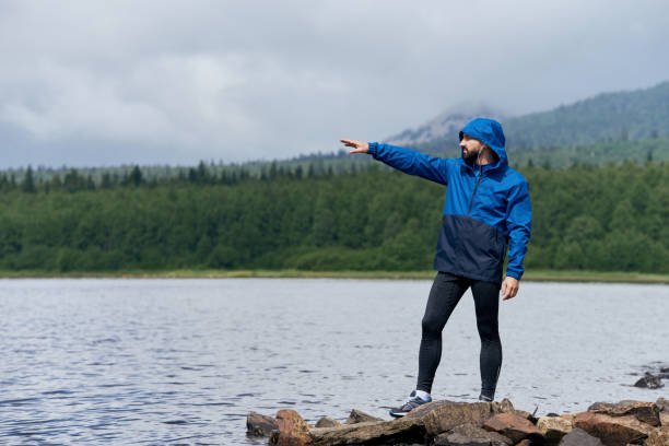 istock Man in blue rain coat pointing finger at rocky river bank 1170273821