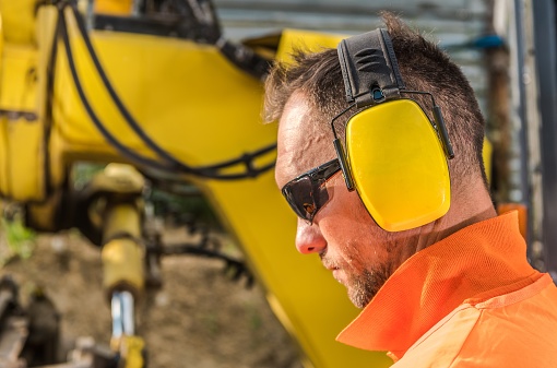 Noise Reduction Hearing Protection Headset. Caucasian Construction Contractor Wearing Sunglasses and Headphones.