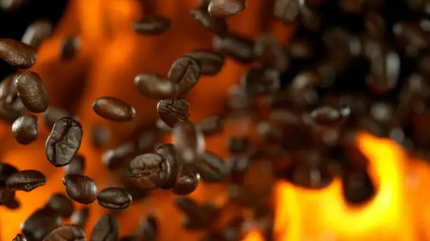 Fresh roasted coffee beans flying in the air in flames, isolated on black background