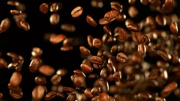 Fresh roasted coffee beans flying in the air, isolated on black background