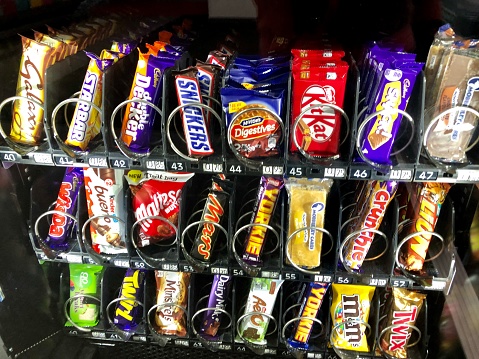 Manchester, Greater Manchester, England, UK - June, 16 2019: Image of chocolate bars, cakes and biscuits in a snack vending machine.