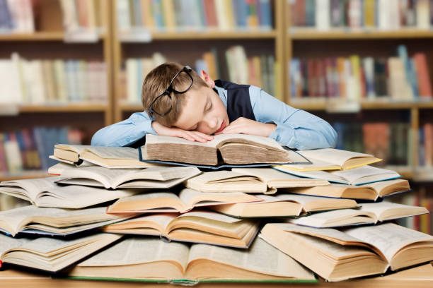 criança tired da escola que dorme em livros, menino furado que estuda na biblioteca, instrução dura - child glasses elementary student reading - fotografias e filmes do acervo