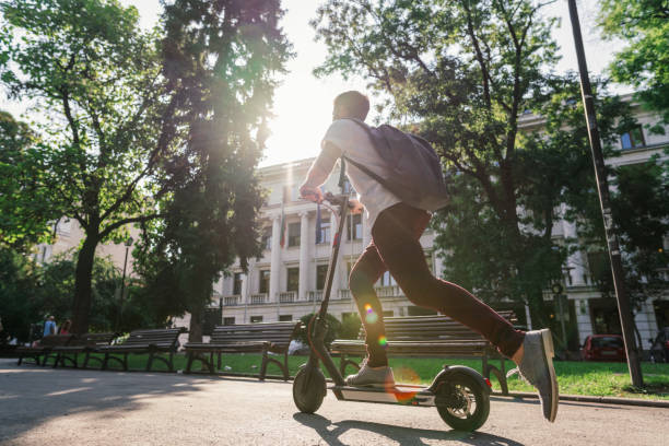 hombre montando e-scooter a través del parque de la ciudad - ciclomotor vehículo de motor fotos fotografías e imágenes de stock