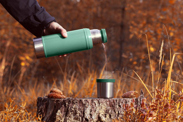 istock A man pours hot tea from a thermos into a mug on a stump. 1170280233