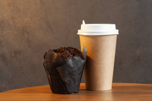 tazza di carta di caffè mattutino e muffin al cioccolato sul tavolo - coffee muffin take out food disposable cup foto e immagini stock