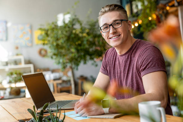 Side view shot of handsome young man looking at camera and smiling while sitting on working place in creative office Men, People, Young Adult, Only Men, Occupation young graphic designer stock pictures, royalty-free photos & images