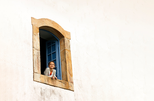 Young Girl leaning in a baroque style window in Caraça Sanctuary (Santuário do Caraça), Minas Gerais, Brazil