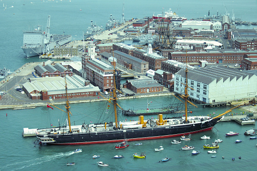 Portsmouth, England - June 11, 2006: Portsmouth Historic Dockyard and Royal Naval Dockyard seen from the top of the Spinnaker Tower. The HMS Warrior is in the foreground and in the middle is the HMS Victory, the Royal Navy flagship. Many recent warships are also docked. Beyond the dockyard is the vast harbour.