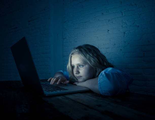 Cute schoolgirl child playing and surfing online late at night. Child addicted to internet games and social media can´t sleep hooked on laptop. Digital technology in childhood and internet addiction. stock photo