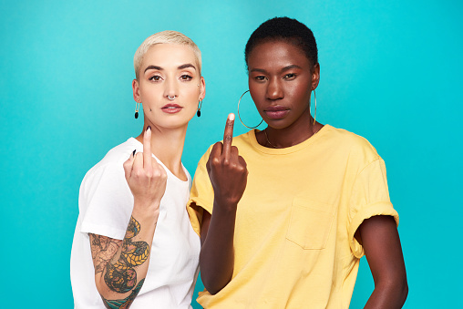 Studio shot of two young women showing their middle fingers against a turquoise background
