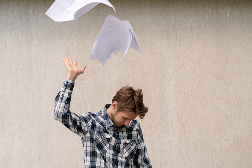 young stressed man throw crumpled paper files in the air, freedom concept