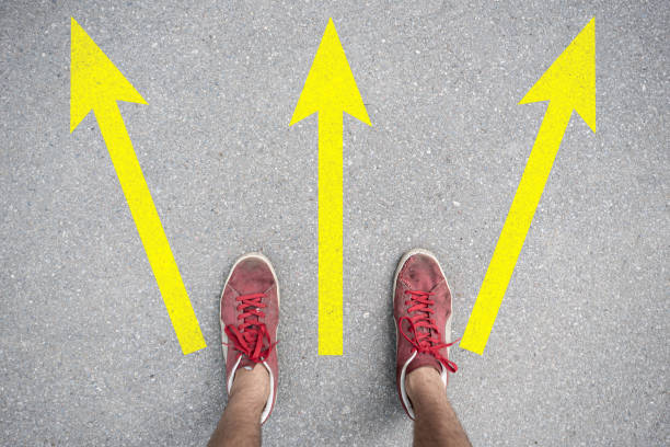 istock difficult to choose where to go, feet stand on the asphalt abstract surface with arrows 1170296564