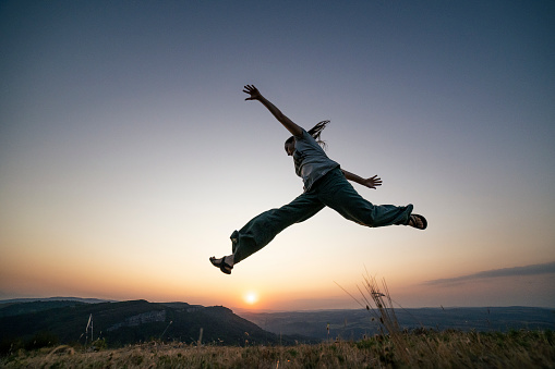 Young man jumping and smiling in front of the sunset.