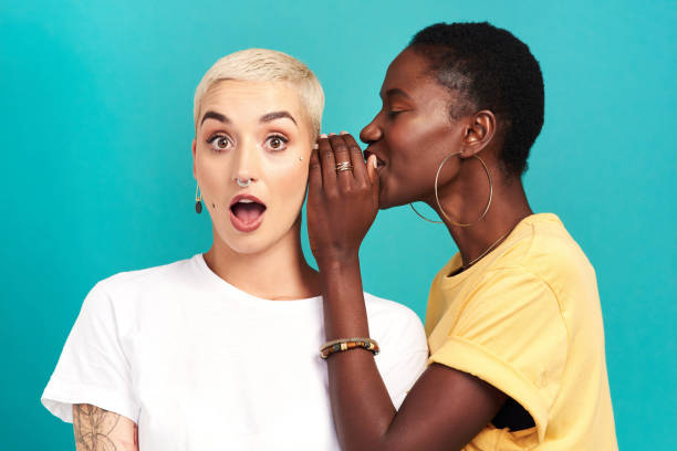 Guess what… Studio shot of a young woman whispering in her friend’s ear against a turquoise background whisperer pictures stock pictures, royalty-free photos & images